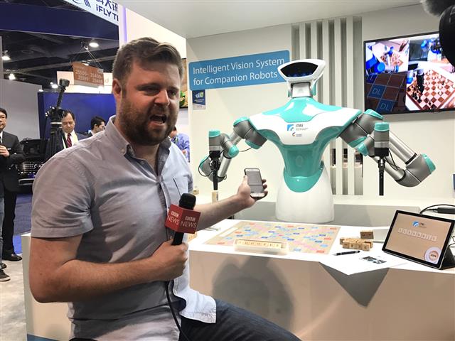 圖2 工研院智慧視覺系統機器人開展即轟動，吸引英國BBC臉書直播與智慧視覺系統機器人玩拼字比賽，吸引9.4萬粉絲觀看。採訪記者Dave Lee盛讚「這大概是CES展覽這麼多展項中最有趣的展出」。