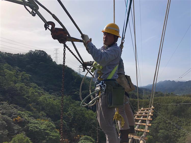 台電員工身著防護設備，在數十公尺高的空中進行緊線作業工程。(1/2)