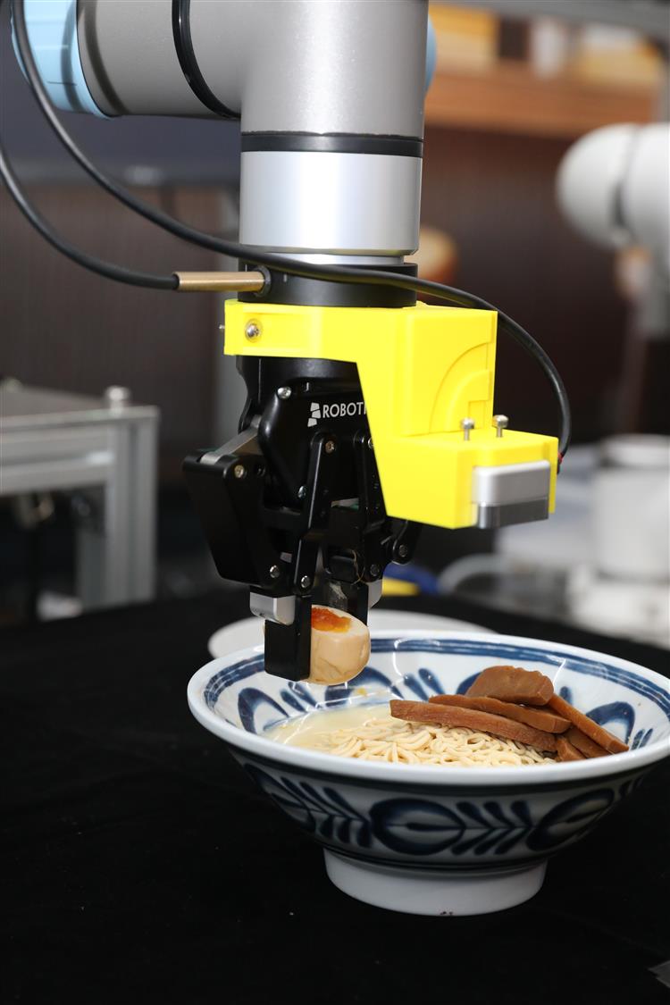 開啟彈跳視窗，連結到工研院展示「AI拉麵機器人」，此技術可自動辨識配料並精準夾料，依指令完成擺盤與出餐，透過AI學習老師傅手藝，提升餐飲效率與品質。(jpg檔)